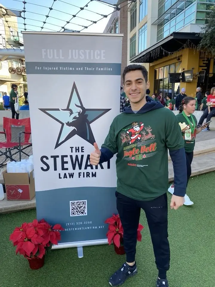 Abraham with The Stewart Law Firm banner at the 2025 Austin Jingle Bell 5K